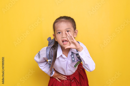 Cheerful Asian schoolgirl in uniform wearing backpack and shout to front making announcement gesture