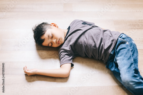 Asian little kid sleeping on the wooden floor at home. Schoolboy fainted on the floor.
