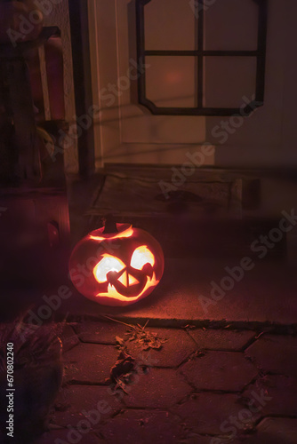 Illuminated Halloween carved pumpkin in front of the door of the house.