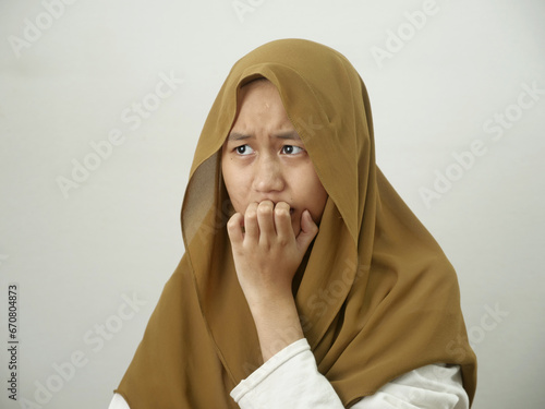 Portrait of Asian muslim teenage girl wearing hijab looked worried and afraid of something bad, biting her nails © airdone