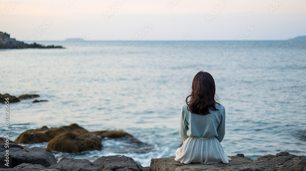 Young woman sitting on the rock by the sea 