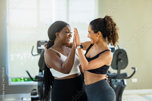 Confident beautiful physical fitness exercise trainer and Overweight black woman in sportswear giving high five to each other in fitness center after workout at the morning.