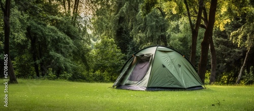 A single tent is set up on the grass surrounded by a lush green landscape of trees