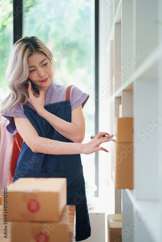 Starting small business entrepreneur of independent Asian female online seller talking on the phone with a customer and packing products for delivery to the customer. and SME delivery concept