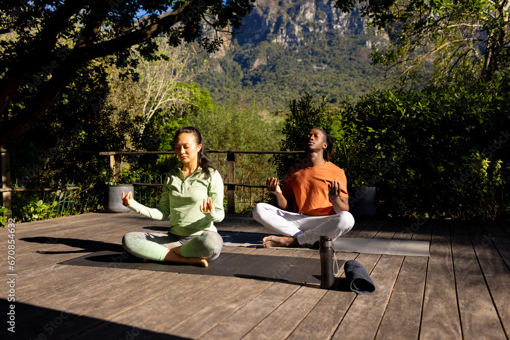 Obraz premium Happy diverse couple practicing yoga meditation sitting on deck in sunny garden, copy space