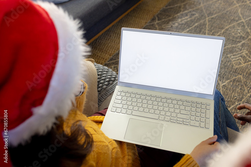 Diverse couple in christmas hats having laptop video call, copy space screen
