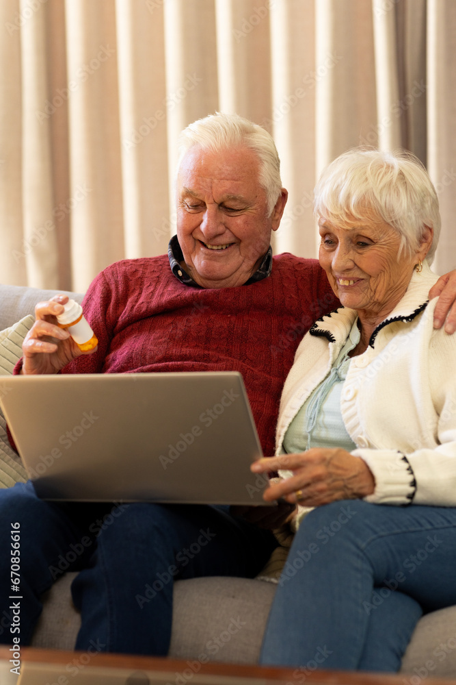 Caucasian senior couple holding pills and having video call in sunny living room