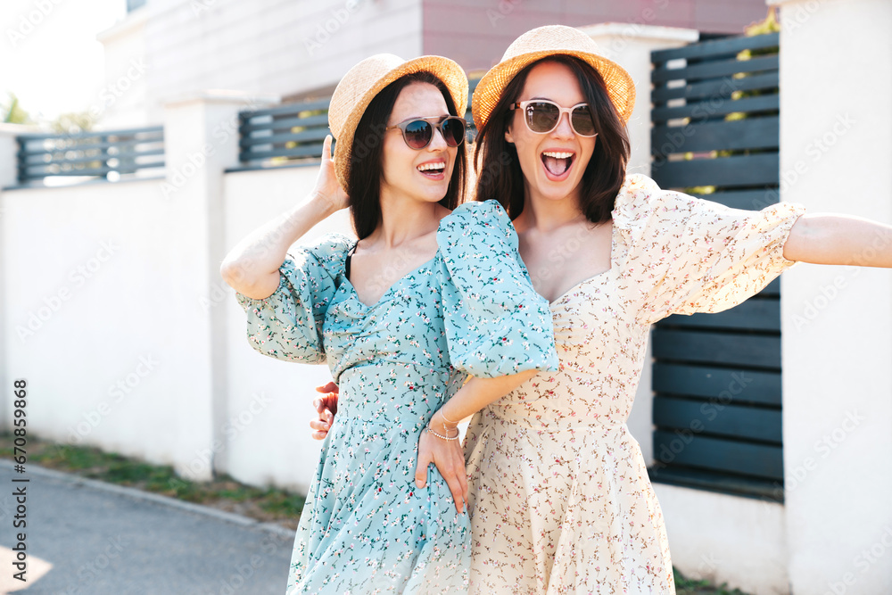 Two young beautiful smiling hipster female in trendy summer dresses clothes. Sexy carefree women posing in the street. Positive models having fun at sunny day. Going crazy. In sunglasses and hat Two young beautiful smiling hipster female in trendy summer dresses clothes. Sexy carefree women posing in the street. Positive models having fun at sunny day. Going crazy. In sunglasses and hat