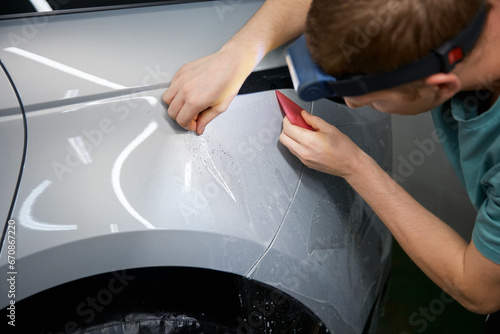 Fotografie Closeup master hand with rubber scraper applying sticking protective film on car