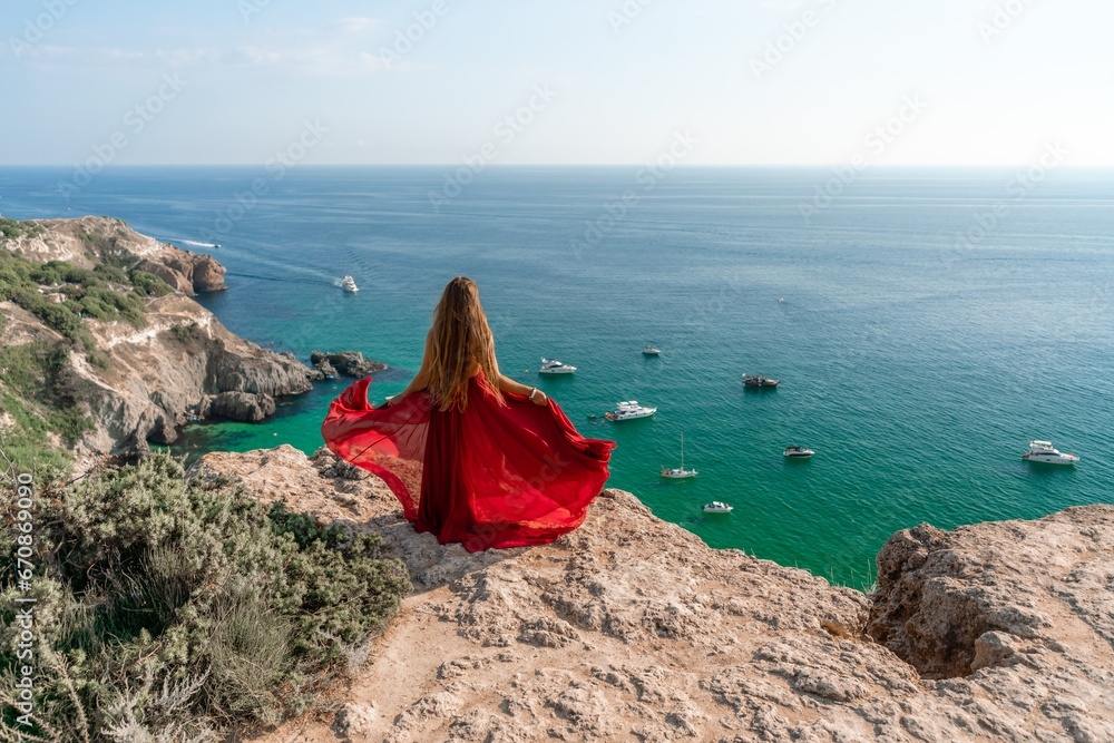 Woman sea red dress yachts. A beautiful woman in a red dress poses on a cliff overlooking the sea on a sunny day. Boats and yachts dot the background.