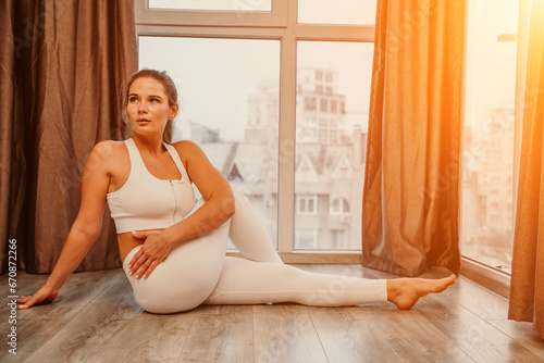 Middle aged athletic attractive woman practicing yoga. Works out at home or in a yoga studio, sportswear, white pants and a full-length top indoors. Healthy lifestyle concept