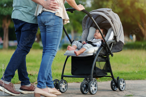 parent (father and mother) pushing infant baby stroller and walking in park.