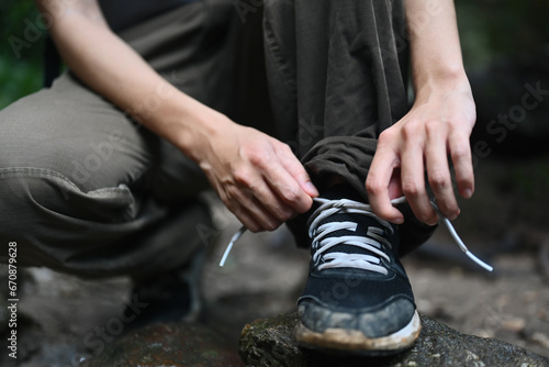 Female hiker tying shoelaces, getting ready walking in forest. Active life, adventure and healthy lifestyle