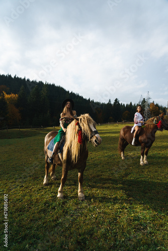 Young women ride horses in national Ukrainian dresses in the Carpathian mountains. Photo session with horses in the mountains. Ukrainian culture concept © Darius