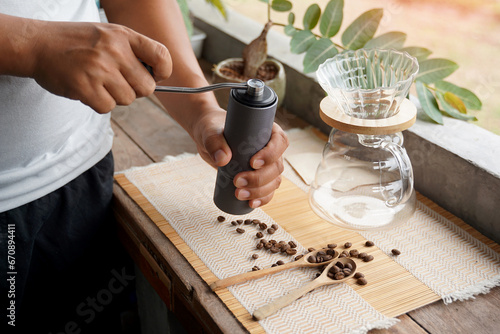 Asian man grinding coffee beans with grinder to easily drip black coffee at home, saving time and getting coffee that has a special aroma and taste. Soft and selective focus. 