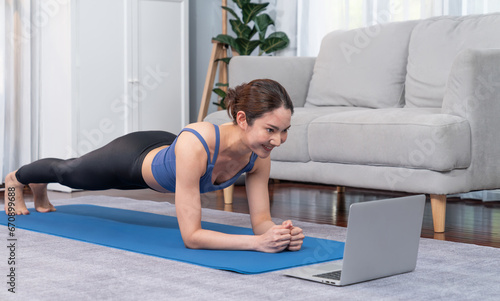 Fit young asian woman planing on the living room floor while following exercise instruction on online training video. Healthy lifestyle workout routine at home. Balance and endurance concept. Vigorous