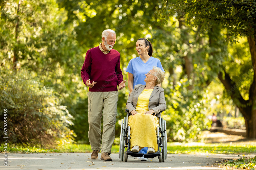 Nursing assistant, senior man and elderly woman in wheelchair enjoying the walk in park. Nursing assistant, senior man and elderly woman in wheelchair enjoying the walk in park.