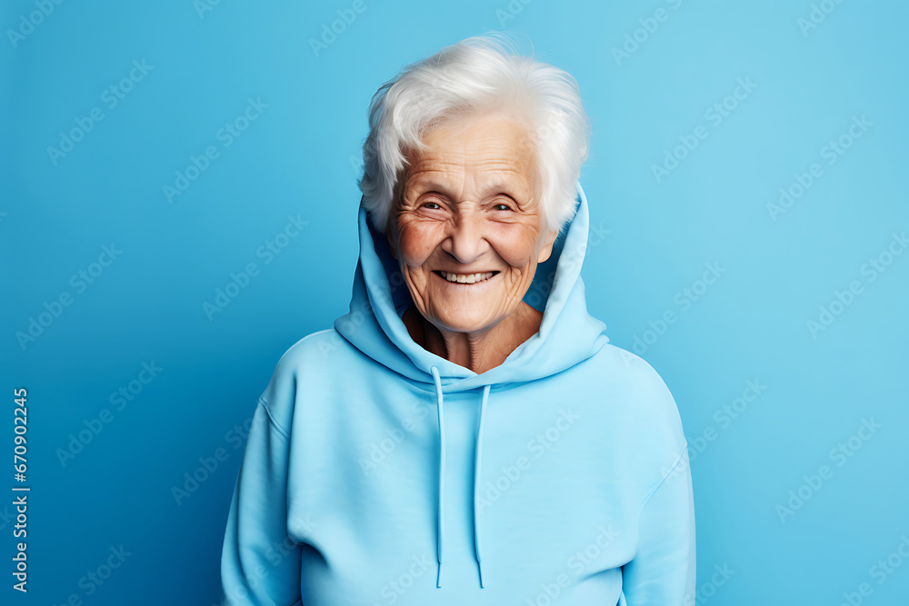 Smiling senior woman posing in blue hoodie on blue background Smiling senior woman posing in blue hoodie on blue background