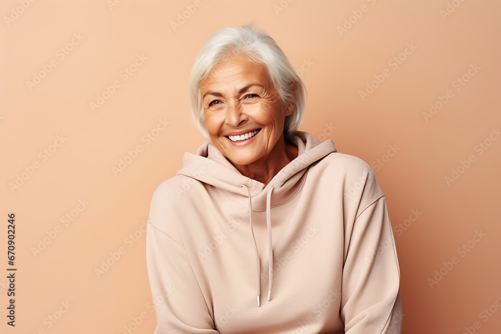 Fototapeta premium Smiling senior woman posing in beige hoodie on peach background