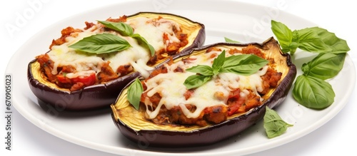 Eggplant filled with vegetables and cheese is baked and garnished with basil leaves It is presented on a white dish with the cooking ingredients arranged nearby on a white background
