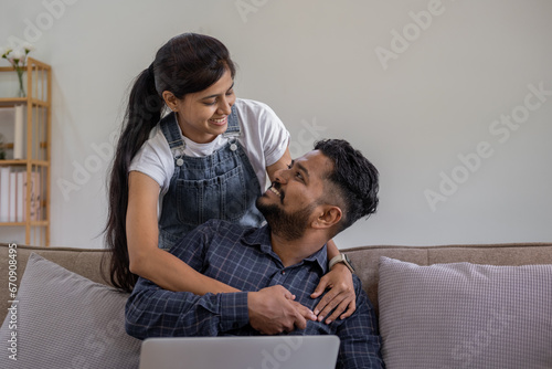 Happy Indian young couple using playing laptop computer notebook on sofa home house