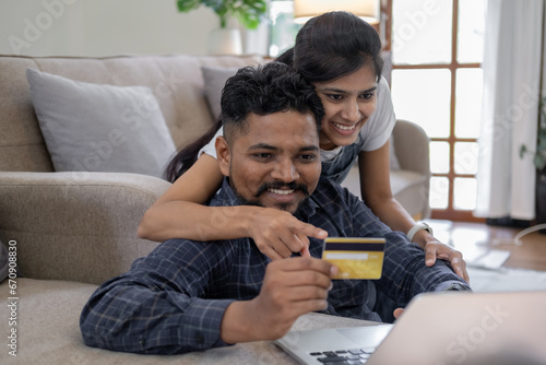 Happy indian couple with bank card and laptop at home, Young caucasian couple smiling happy using laptop and credit card