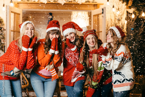 A group of cheerful girls in Santa hats against the background of a wooden house with garlands