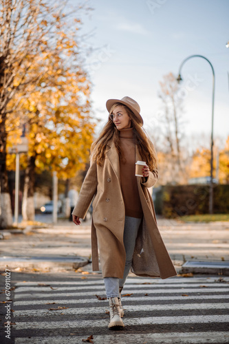 A beautiful adult woman in a coat and hat walks on the road in the middle of the city in the autumn season