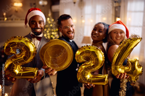 Happy multiracial friends with 2024 golden balloons on New Year's party at home looking at camera.