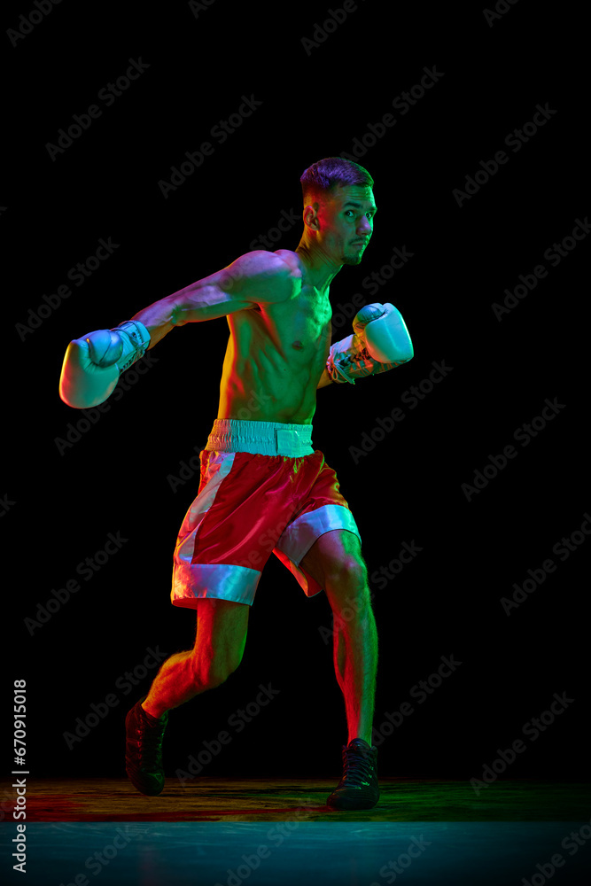 Active shirtless boxer, mixed martial art fighter exercising before fight against black mode background in mixed neon filter, light.