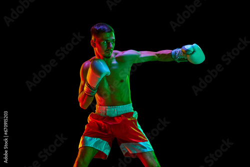 Talented shirtless boxer, mixed martial art fighter who preparing to fight against black mode background in mixed neon filter, light.