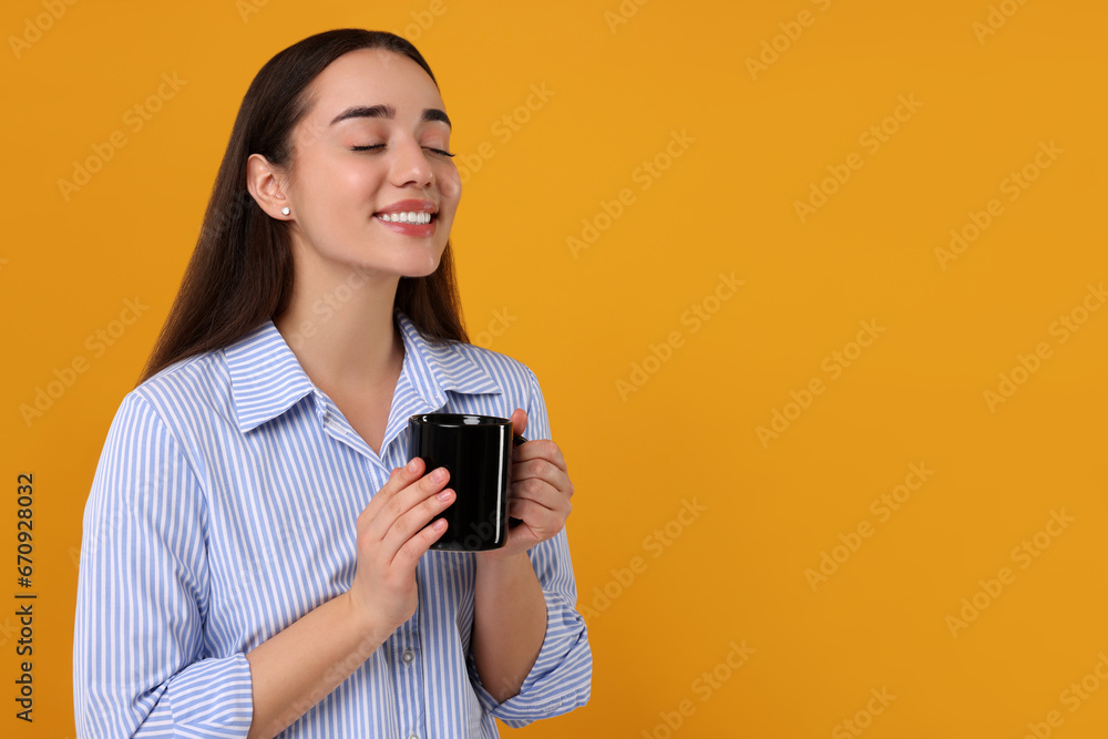 Happy young woman holding black ceramic mug on orange background, space for text Happy young woman holding black ceramic mug on orange background, space for text
