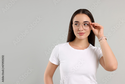 Beautiful woman wearing glasses on light gray background, space for text