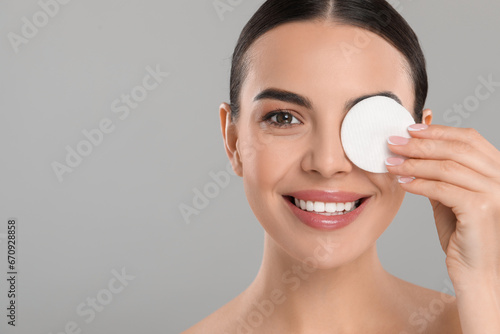 Beautiful woman removing makeup with cotton pad on light grey background. Space for text