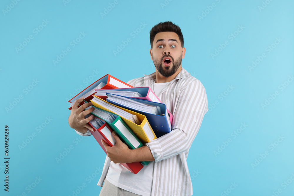 Shocked man with folders on light blue background Shocked man with folders on light blue background