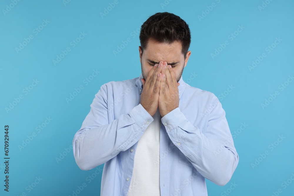 Resentful man covering face with hands on light blue background Resentful man covering face with hands on light blue background