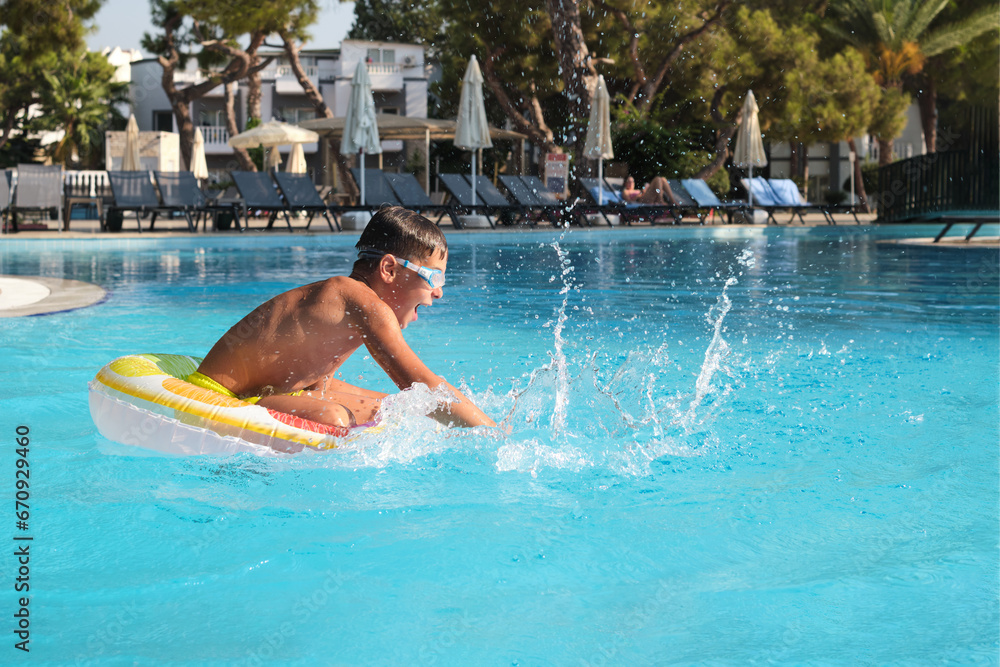 Modern vacation scene: kid in motion in a pristine resort pool with deck chairs in view
