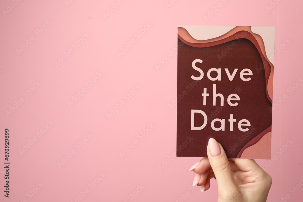 Woman holding beautiful card with Save the Date phrase on pink background, closeup. Space for text Woman holding beautiful card with Save the Date phrase on pink background, closeup. Space for text