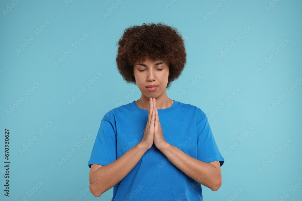 Woman with clasped hands praying to God on light blue background Woman with clasped hands praying to God on light blue background