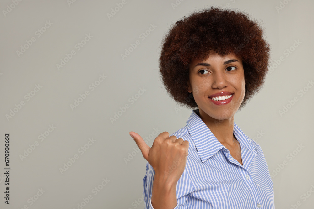 Happy young woman pointing at something on grey background. Space for text Happy young woman pointing at something on grey background. Space for text