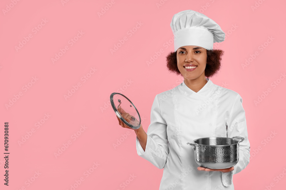 Happy female chef in uniform holding cooking pot on pink background. Space for text Happy female chef in uniform holding cooking pot on pink background. Space for text
