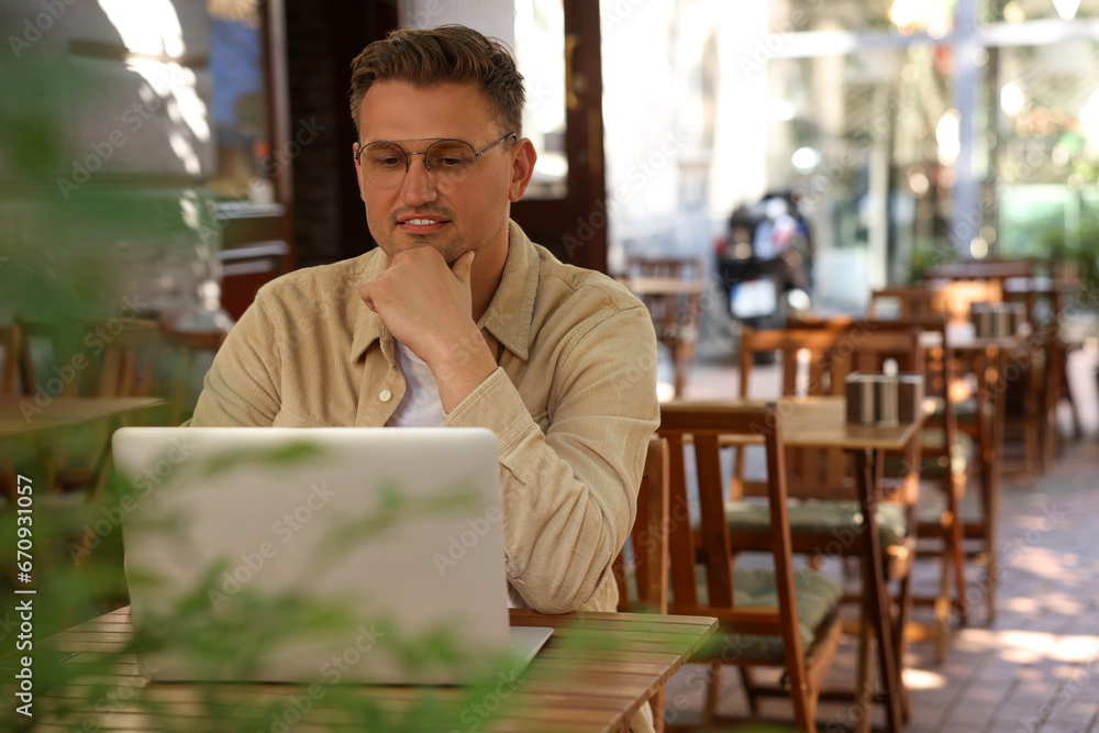 Handsome man working on laptop at table in outdoor cafe. Space for text Handsome man working on laptop at table in outdoor cafe. Space for text