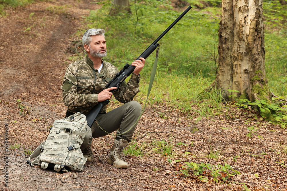 Man with hunting rifle and backpack wearing camouflage in forest. Space for text Man with hunting rifle and backpack wearing camouflage in forest. Space for text