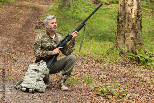 Man with hunting rifle and backpack wearing camouflage in forest. Space for text