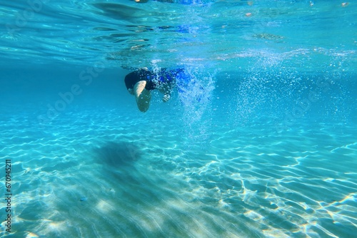 Fototapeta Naklejka Na Ścianę i Meble -  Girl snorkeling and swimming with fins in the shallow turquoise sea, sandy seabed. Crystal clear blue water with swimmer. Activity in the water, sun reflections, underwater photography.