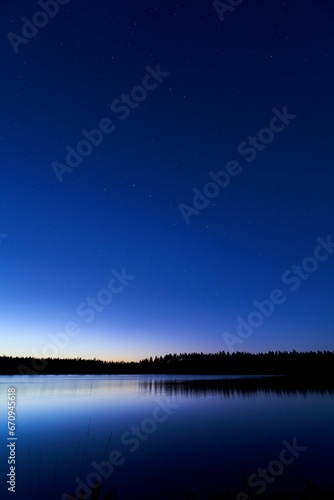 the night sky is lit up over a lake in the woods © Wirestock