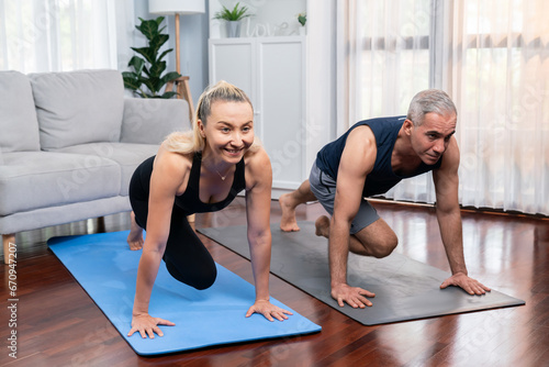 Fototapeta Naklejka Na Ścianę i Meble -  Athletic and active senior couple doing exercise on fit mat with plank climbing together at home exercise as concept of healthy fit body lifestyle after retirement. Clout