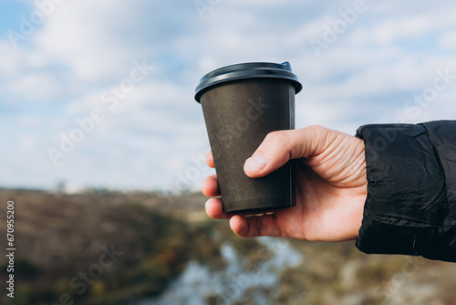 Black paper coffee cup in hand. Drinking take away coffee outdoors. Freedom travel concept. photo