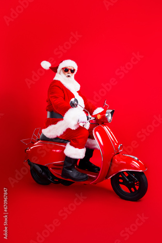 Full size photo of astonished funny grandfather wear trendy santa costume glasses riding fast on moped isolated on red color background