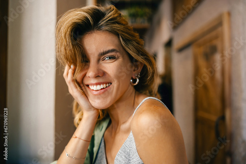 /Happy stylish good-looking lady with wonderful smile is touching her chin, looking at camera and enjoying sunny day n cafeteria 